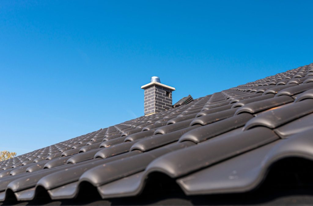 Black tiled roof with brick chimney and blue sky