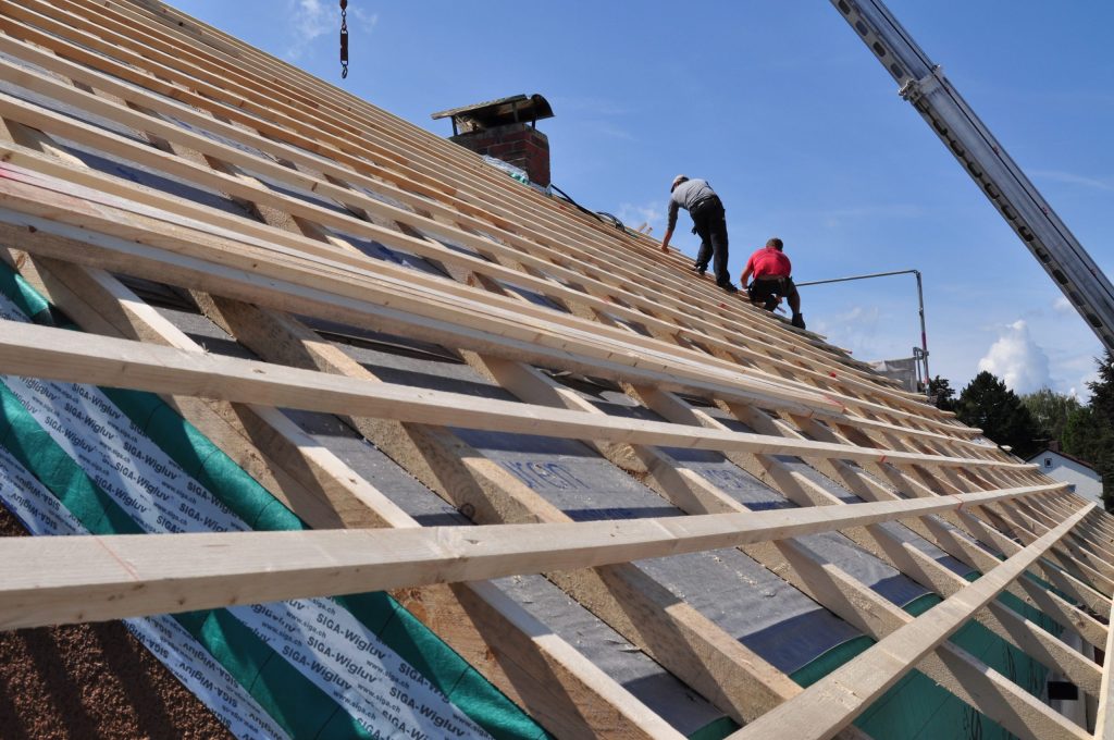 Workers installing wooden roof framework outdoors